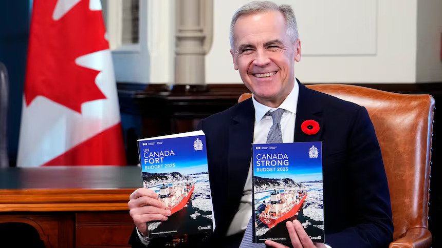 Prime Minister Mark Carney holding the budget documents, with the Canadian flag in the background