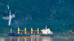 A cargo ship with the name 'Pacific Basin' sails by a scenic waterfall in Squamish, BC, Canada